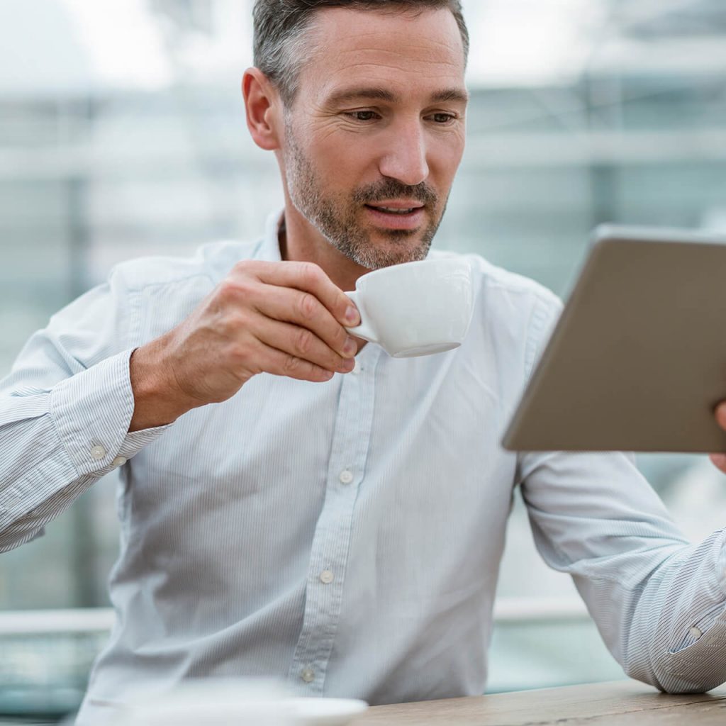 Geschäftsführer schaut auf sein Tablet und hält eine Tasse vor seinen offenen Mund